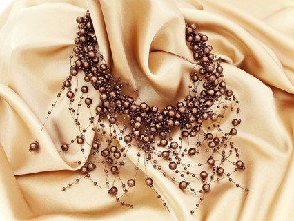 Fashion brown necklace in chaplet shape over golden textile background