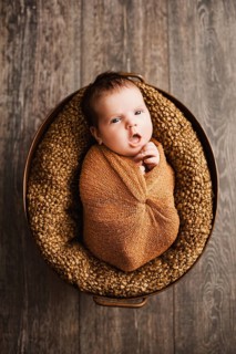 Baby boy in a brown wrap is yawning at a newborn photo shoot.