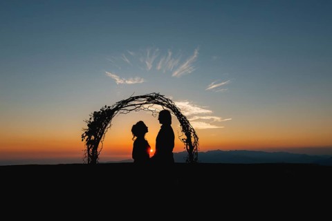 Silhouettes of bride and groom holding hands near the wedding arch at sunset at the wedding
