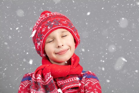 Dreamy child in warm clothing against a winter background. A boy with a red knitted hat and closed