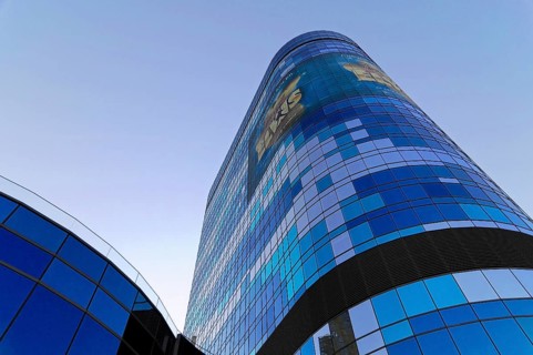 A modern skyscraper with a blue reflective glass facade and advertising, illuminated in daylight,