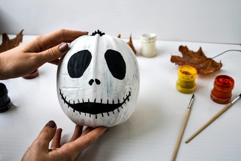 Woman paints face on orange pumpkin for Halloween. Autumn leaves. Diy children craft. Do it