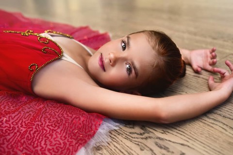 Side view portrait of a cute Beautiful little ballerina in a performance dress lying on the floor