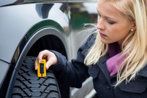 A young woman measures the tread depth of her car tyre. The right depth in the tread of a tyre can