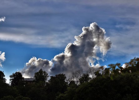Threatening thundercloud grows behind a house into the blue sky, dramatic cloud formation, Upper