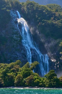 Waterfall cascades over a wooded slope and sprays fine spray into turquoise-coloured water, summer,