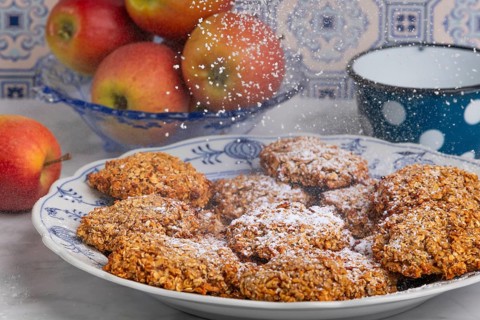 Freshly baked oat biscuits on a plate are sprinkled with sugar, apples in the background