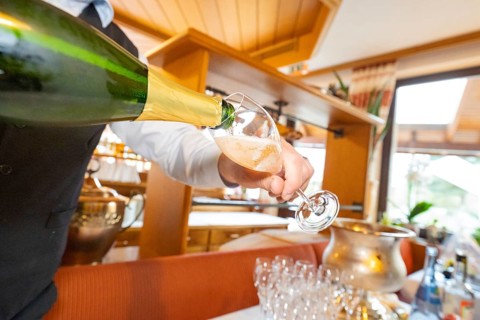 A waiter pours white wine into a glass, wooden decor in the background, Europäischer Hof,