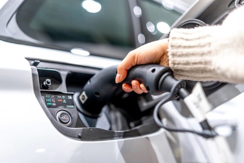Close up of a hand plugging a charging cable into an electric vehicle at a car dealership,
