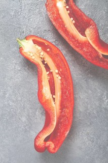 Fresh red peppers are sliced to reveal their bright interior, showcasing seeds and texture. The