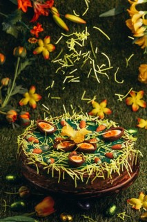 Easter grass falls on Easter cake with carrots and chocolate eggs surrounded by flowers in green