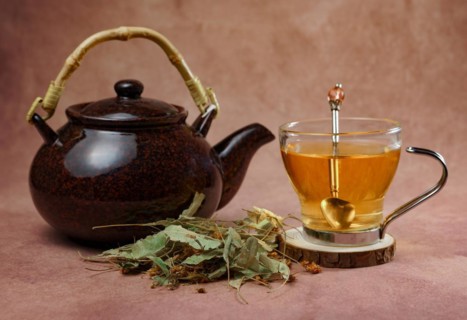Glass cup with teapot and fresh linden leaves, infusion of lime blossom tea, medicinal plant with