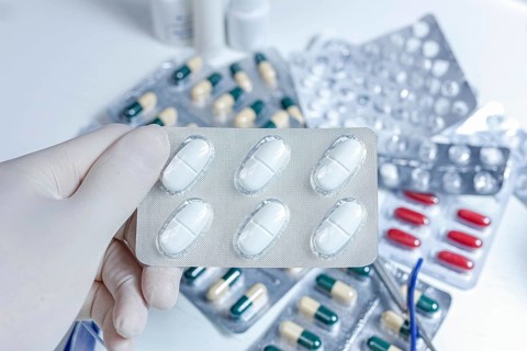 A gloved hand holding a blister pack of white pills amidst various capsules