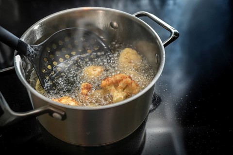 Deep frying cauliflower florets in a pot with boiling cooking oil on the stove, preparation of a