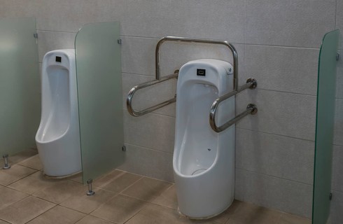 Porcelain urinal with handrails for use by disabled person next to non-disabled urinal in public