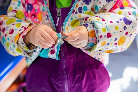Close up shot on the hands of a kindergarten child struggling to latch and close the zipper of his