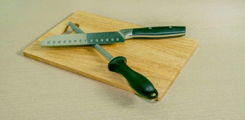 Santoku knife and honing steel on woodblock cutting board with light wood grain background