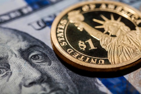 One dollar coin, The Statue of Liberty, on hundred dollars bills. Closeup, macro shot