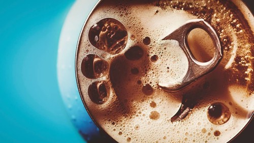 Frothing beer, cola or energy drink from open can, top view, copy space