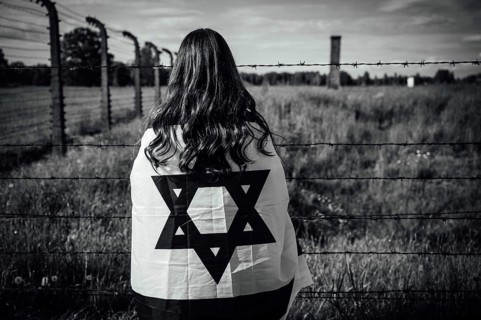 Jewish girl with Israeli flag by the fence of the concentration camp
