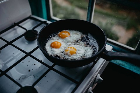 Frying pan with three eggs cooking on a gas stove beside a window