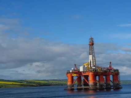 A single oil drilling platform sits in the calm sea with a slightly cloudy landscape behind it,