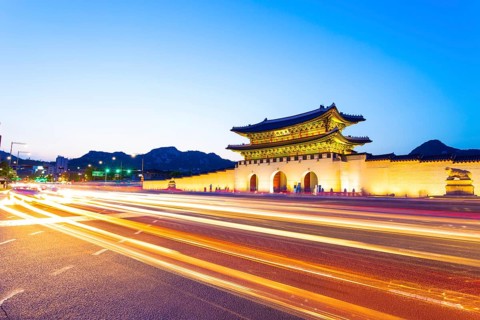 Colorful streaking headlights of cars passing in front of lighted gate of Gwanghuamun, entrance to
