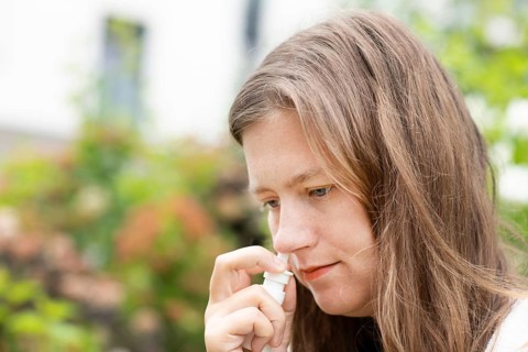 Young woman suffers from hay fever and sprays her nose outdoors, Freiburg, Baden-Württemberg,