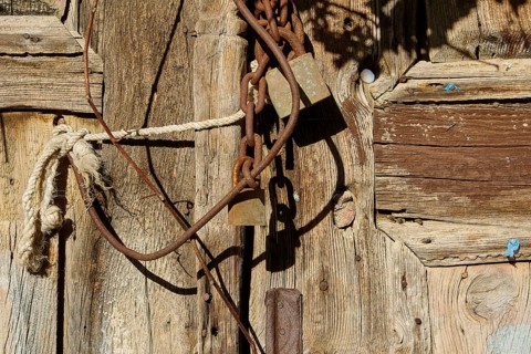 Old wooden door with rusty chains and locks, weathered in the sunlight, Symi Town, Symi,