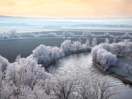 View of the river Unstrut in the Unstrut valley in winter at dawn, fields and trees covered with