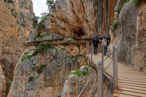 People with helmets walking on the wooden path Caminito del Rey along a rocky cliff, Malaga, Spain,