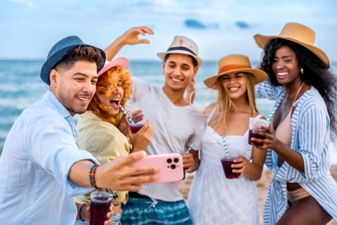 Multi ethnic friends taking selfie on beach while drinking juice, enjoying summer vacation together