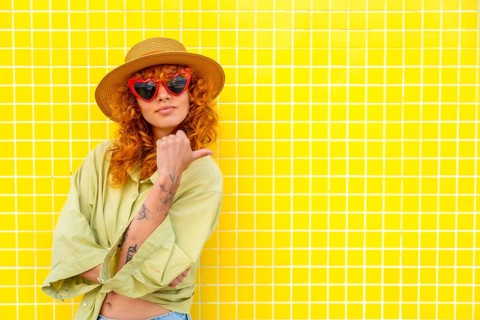 Fashionable influencer posing confidently against a vibrant yellow tiled wall, pointing with her