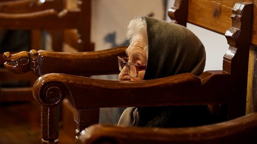 An elderly woman with a hood, sitting in a chair, deep in thought, Easter 2025, Church of the