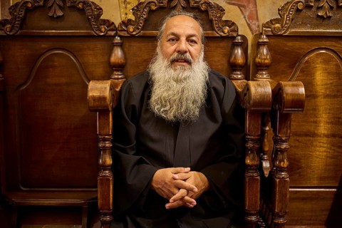 Papas Nektarios, Elderly man with beard on a wooden chair in a quiet, monastic environment,