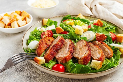Caesar salad, with duck breast, on a light plate, on a light background, homemade, no people