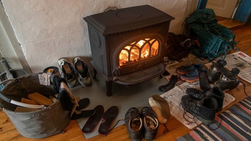 Drying wet hiking boots in front of a burning wood-burning stove, Fokstugu farm, Fjellstue,