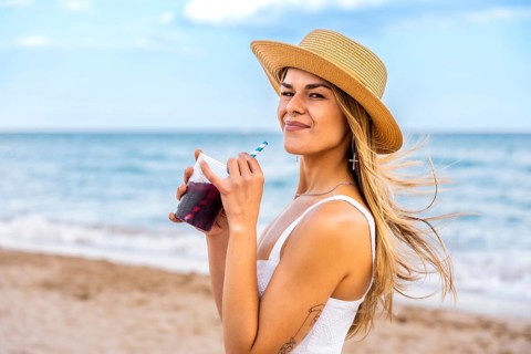 Young woman in a straw hat enjoying a refreshing drink while relaxing on the beach, soaking up the