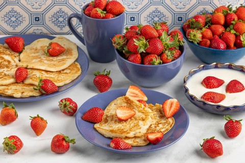 Pancakes and fresh strawberries on plates with yoghurt, blue crockery