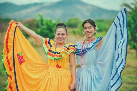 Portrait of two Hispanic women wearing cultural folkloric costume in a field. Two smiling Hispanic