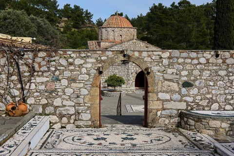 Path of mosaic stones leads to a church, surrounded by a high stone wall and trees, Thari