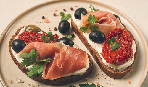 Sandwiches with cheese and prosciutto, dried tomatoes and olives, breakfast on a plate