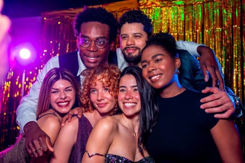 Group of cheerful elegant friends posing together for a photo at nightclub party with disco lights