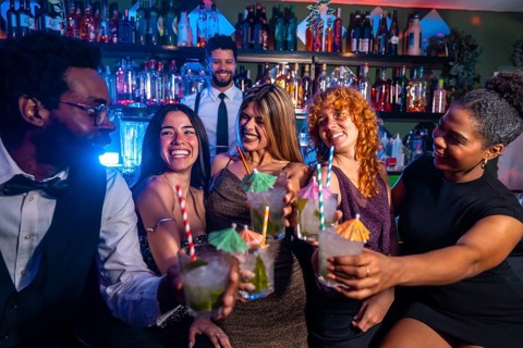 Cheerful multi ethnic friends raising cocktail glasses for a celebratory toast in a nightclub,