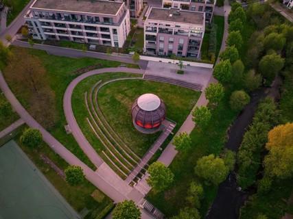 Aerial view of a modern wooden construction in the park with trees and surrounding buildings at