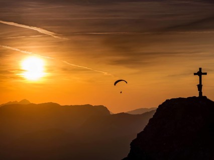 Paraglider flying next to the summit cross of the small Jenner at sunset, Reiteralpe in the