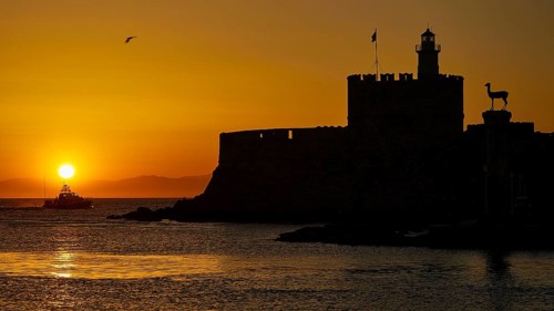 A boat glides in front of the silhouette of a fortress in the warm sunrise, dawn, Fort of Saint