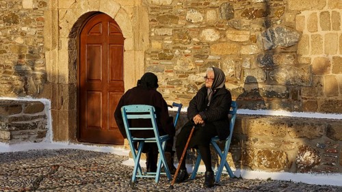 Two elderly people sitting on blue chairs in front of a stone wall and talking, Easter 2025, Church