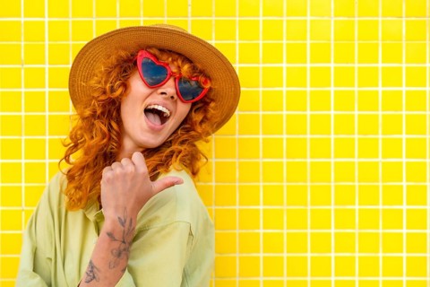 Cheerful influencer pointing her thumb while smiling, wearing a straw hat and heart shaped