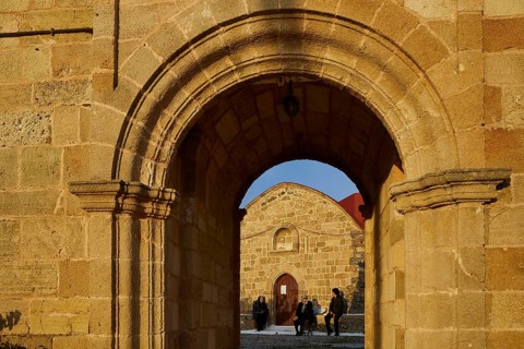 View through a stone arch onto people sitting and chatting in front of a church, Easter 2025,